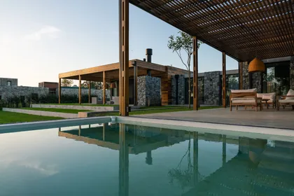 Piscina moderna junto a casa con paredes de piedra y pérgola de madera — proyecto CASA AH, por Rastro Estudio, en Chapadmalal