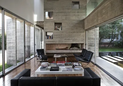 Living con doble altura, hogar central y amplios ventanales al jardin — proyecto Casa Torcuato, por Luciano Kruk