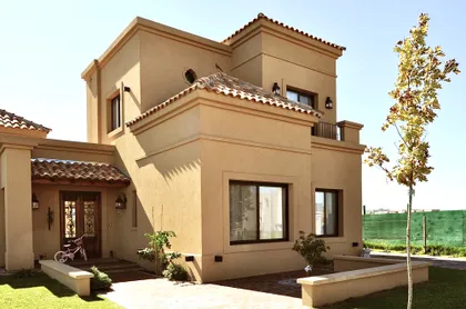 Fachada residencial estilo mediterráneo beige con techos de terracota y jardín — proyecto San Marcos, por Marconi Silva Arquitectos, en Benavidez