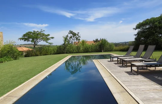 Pileta espejo con deck de madera y jardín verde extenso — proyecto Residencia PZ, por Gil Fialho