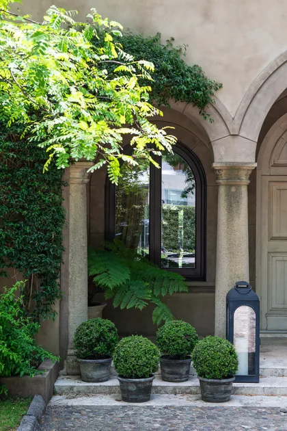 Patio con arcos de piedra, plantas en macetas y vegetación frondosa — proyecto Casa Toscana , por Estudio Du