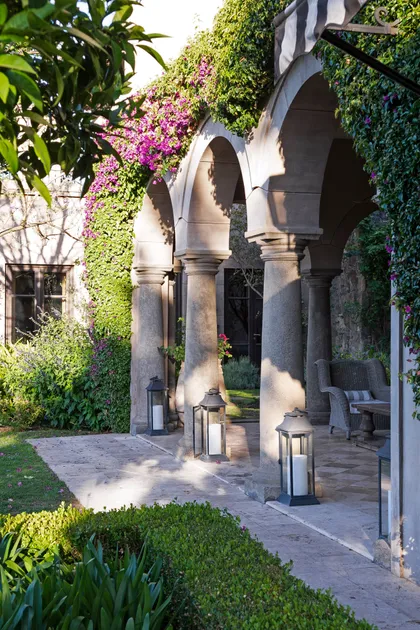 Galería con arcos de piedra, columnas y enredaderas con flores fucsia — proyecto Casa Toscana , por Estudio Du 