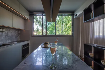Cocina moderna con isla de mármol gris y grandes ventanales verdes — proyecto Residencia TS, por Karina Vinocur