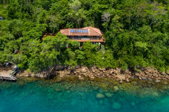 Casa moderna con paneles solares frente al mar turquesa rodeada de selva — proyecto Casa da Ilha, por Miguel Capanema Arquitetura