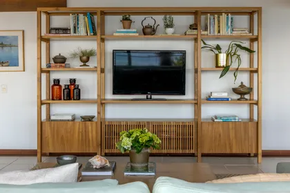 Mueble TV de madera clara con estantes, plantas y libros decorativos — proyecto Casa da Ilha, por Miguel Capanema Arquitetura