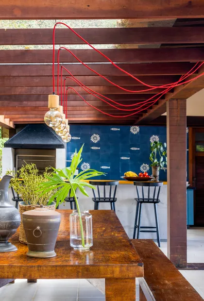 Quincho moderno con pergola roja, mesada madera y pared azul decorada — proyecto Casa da Ilha, por Miguel Capanema Arquitetura