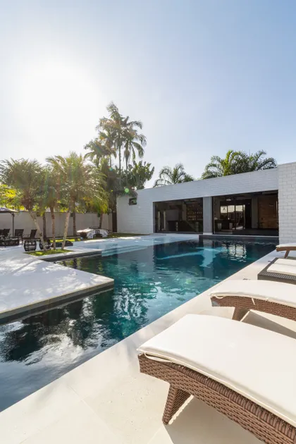 Pileta moderna con deck, sillones y palmeras en exterior residencial — proyecto Mansão de Gabigol, por Carlos Pardal, en Guarujá