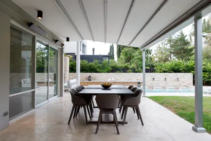 Comedor exterior moderno con mesa de madera oscura y sillas grises bajo toldo retráctil — proyecto TOLDER - PERGOLAS, por Argentina en Obra 2024, en Rincón de Milberg