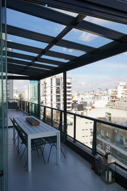 Terraza moderna con techo de vidrio y vista a la ciudad — proyecto TOLDER - TECHOS DE VIDRIO, por Argentina en Obra 2024, en Rincón de Milberg