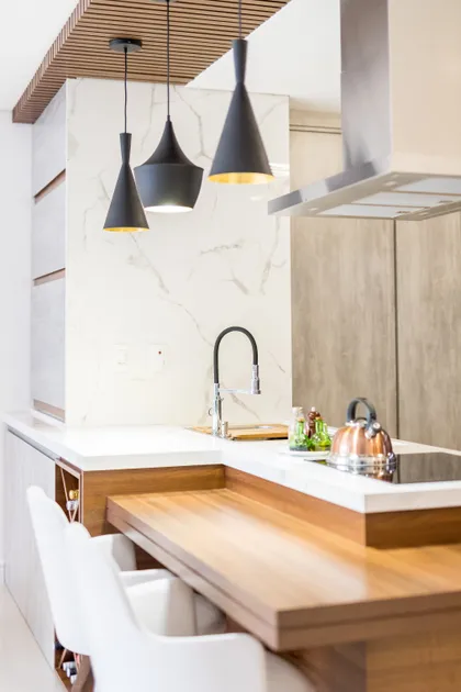 Cocina moderna con isla de madera, mesada blanca y lámparas negras colgantes — proyecto Apto Sérgio e Lizandra, por Coletivo Arquitetura