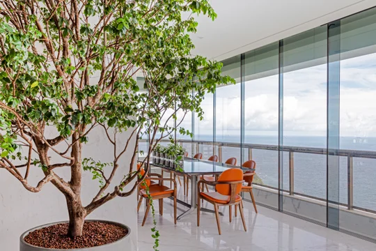 Balcón alto con árbol interior, sillas naranjas y vistas al horizonte — proyecto Apto S | A, por Arquitetura Paulo Melo E Paulo