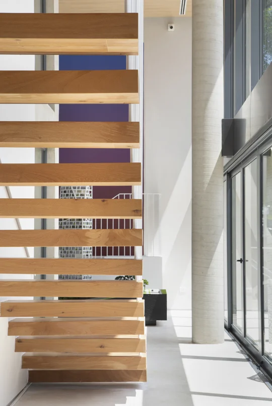 Escalera volada madera en hall luminoso con piso hormigón y ventanal — proyecto Stand Age 360, por GabrielaCasagrande Arquitetura