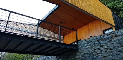 Casa moderna con fachada de madera y piedra, pasarela elevada y tragaluz — proyecto Casa Península San Pedro, por Servente Larrazabal Arq, en Bariloche