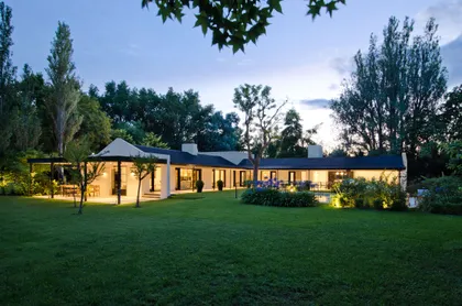 casa moderna con iluminación de jardín y césped extenso — proyecto Casa BA, por Estudio Dado, en Pilar