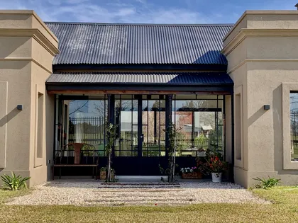 fachada principal de casa moderna con galeria y techo de chapa — proyecto Los Jazmines Pilar del Este, por Marconi Silva Arquitectos, en Pilar del Este