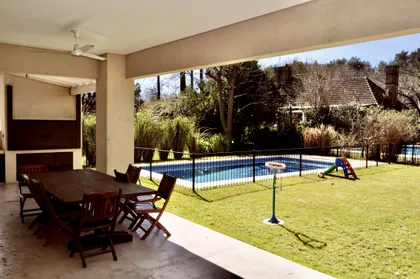 Galería techada con gran mesa de madera y vista a pileta y jardín — proyecto Newman Benavidez, por Marconi Silva Arquitectos, en Benavidez