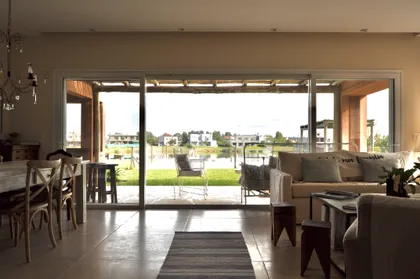 Living moderno con ventanal amplio y vista a lago y casas — proyecto Santa Teresa, Villanueva, por Marconi Silva Arquitectos, en Benavidez