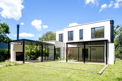 Casa moderna blanca con pérgola negra, jardín y parrilla exterior — proyecto Bosque Chico, por Estudio Arq. María Sioli, en Garin