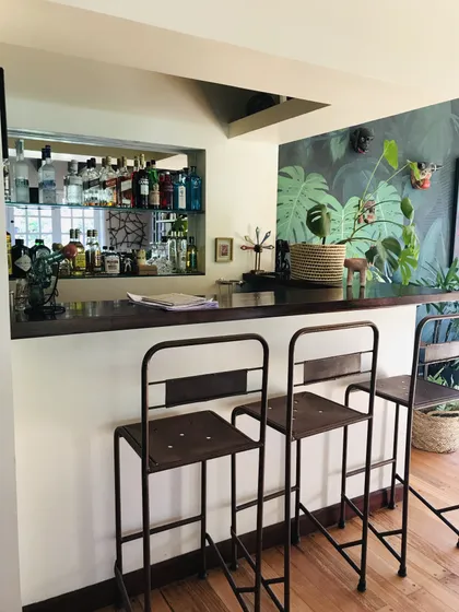Barra de cocina con estantes, papel tapiz tropical y banquetas industriales — proyecto Monroe - La Horqueta, por Mgc.arq, en La Horqueta