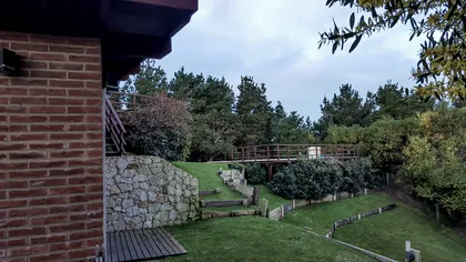 Fachada rústica con detalles en piedra y ladrillo, rodeada de jardín — proyecto Vivienda Unifamiliar en Costa Esmeralda, por Estudio Schifano, en Costa Esmeralda