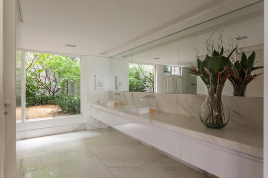 Baño minimalista blanco con mesada de mármol y ventanal al jardín — proyecto APARTAMENTO FL, por Frederico Bicalho Arquitetura