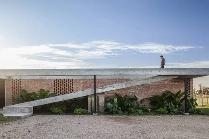 Fachada moderna de ladrillo con pasarela de hormigón y vegetación — proyecto Casa Volt, por Estudio PK, en Capilla del Señor
