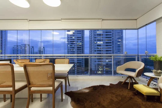 Terraza con vista panorámica a rascacielos al atardecer, muebles de madera y cuero — proyecto Varandas, por Xico Diniz