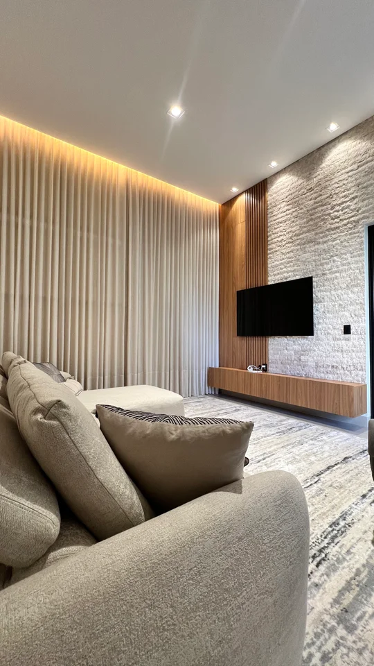 living moderno con sillón beige, TV y pared de piedra iluminada — proyecto Residência H&N, por Gaby Boing Arquiteta, en Alta Floresta