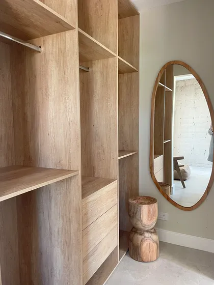 Amplio vestidor de madera natural con espejo ovalado y taburete tallado — proyecto El Secreto, por Grupo Pauta Arquitectura, en Tigre