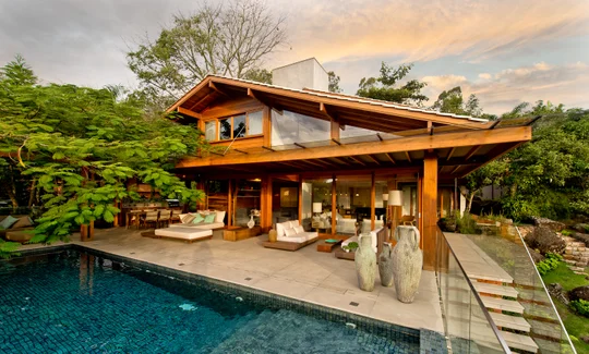 Casa moderna de madera con pileta, deck y vegetación exuberante al atardecer — proyecto Casa A.L., por Ruschel Arquitetura e Urbanism