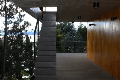 moderna escalera metálica flotante sobre deck de madera — proyecto Casa Península San Pedro, por Servente Larrazabal Arq, en Bariloche