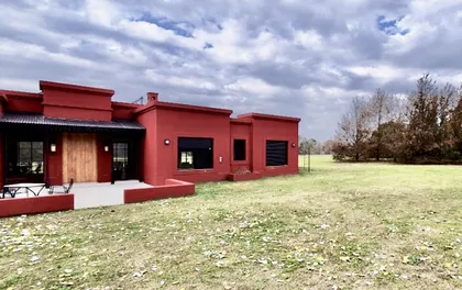 Casa moderna con fachada terracota y ventanales sobre un jardín — proyecto Las Vizcachas, por Marconi Silva Arquitectos, en Los Cardales
