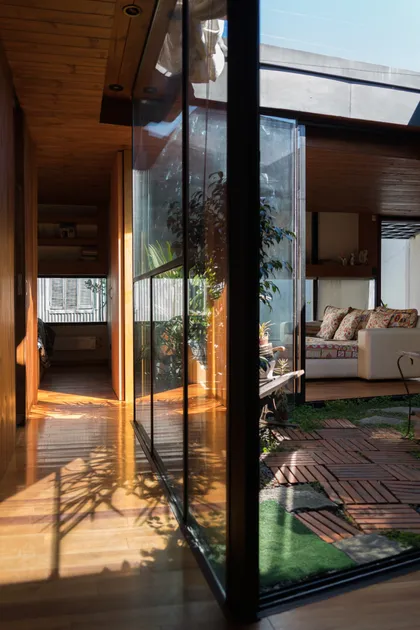 Pasillo moderno con suelo de madera, cerramiento de vidrio y jardín interior — proyecto PH M, por LOI Arquitectura, en CABA