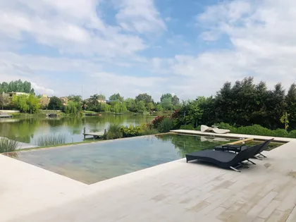 Piscina infinita moderna con tumbonas y vista al lago — proyecto SANTA BARBARA , por Greschek Obras , en Benavidez