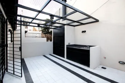 Quincho moderno con parrilla y bacha, techo de pérgola metálica negra — proyecto PH Bustamante, por Escalante Vela Arquitectos, en CABA