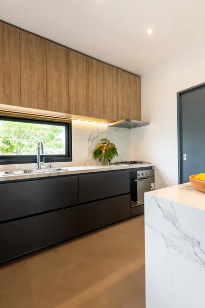 Cocina moderna con muebles de madera y mármol, ventana al jardín — proyecto Santa Isabel - Andrea Gonzalez, por ABEJA CONCEPT, en Nordelta
