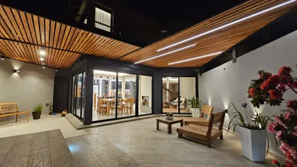 Patio nocturno con pérgola madera, ventanales negros y flores — proyecto Timeless House, por Estudio UFV72, en B1602 Florida