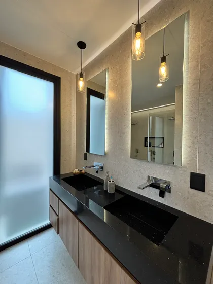 Baño moderno con doble bacha, mesada de piedra negra y luces colgantes — proyecto LOTE 020, por DIKKA Arquitecta , en San Vicente