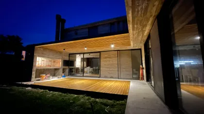 Moderno patio con deck y fachada de hormigón de noche — proyecto Casa R2, por Guerrero Arquitectos, en Pinamar