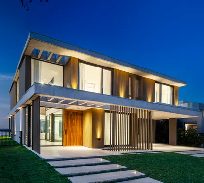 Fachada moderna de noche con madera vertical y amplios ventanales — proyecto CASA MUELLES 239, por ABAD GADANO, en Belén de Escobar