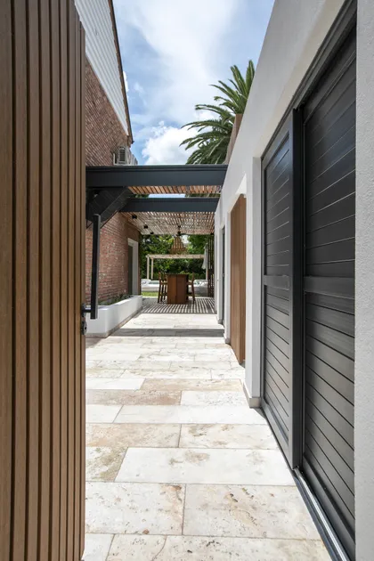 Patio moderno con mesa de madera bajo pérgola y suelo de piedra — proyecto Obra La Posta, por Arq. Lourdes Yarade Saravia, en Pilar