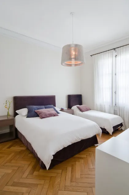 Dormitorio con dos camas, suelo de madera y lámpara colgante — proyecto Dpto LH, por Estudio Dado, en Recoleta