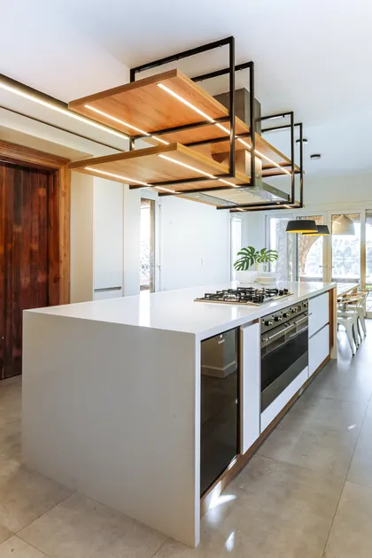 Cocina moderna con isla central, luminarias suspendidas madera y acero negro — proyecto Casa Nordelta, por Gutman+Lehrer Arquitectas, en Nordelta