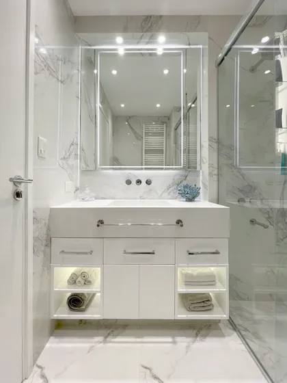 Baño minimalista con vanitory blanco, espejo iluminado y mármol — proyecto Remodelación Baño, por Estudio Nicolás Pierry
