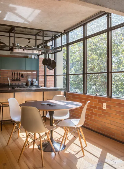 Comedor industrial con mesa redonda y ventanal sobre jardin — proyecto Apartamento SQN 410, por Coda Arquitetos