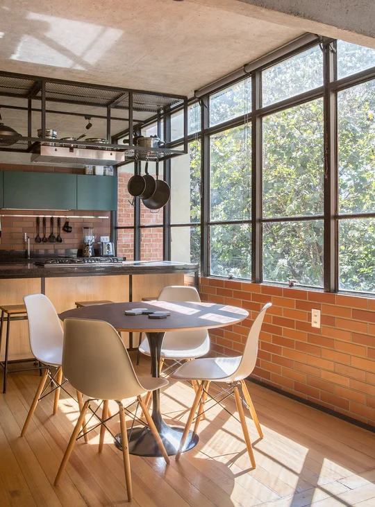 Comedor industrial con mesa redonda y ventanal sobre jardin — proyecto Apartamento SQN 410, por Coda Arquitetos