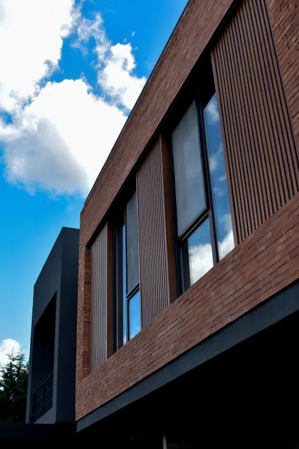 Fachada moderna con ladrillo, madera y grandes ventanales negros — proyecto CASA HC, por Daniel Daniele - Oficina de Arquitectura, en Canning
