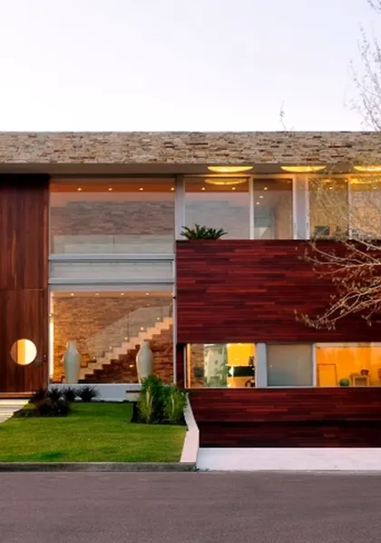 Fachada moderna de madera oscura y piedra con grandes ventanales — proyecto Casa Cinta, por Barrionuevo Arquitects, en B2814 Los Cardales