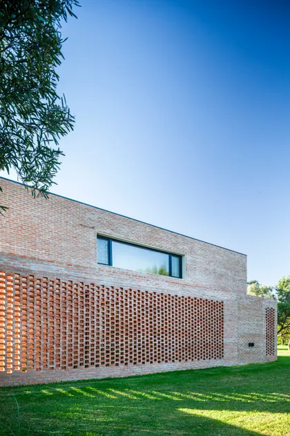 Fachada moderna de ladrillo visto con pantalla de ladrillo perforado y ventana alargada — proyecto Casa Brick, por LSA. , en Pilar