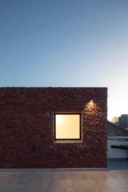 Fachada de ladrillo con ventana iluminada y cielo azul — proyecto PH Helguera, por OADD arquitectos, en Buenos Aires